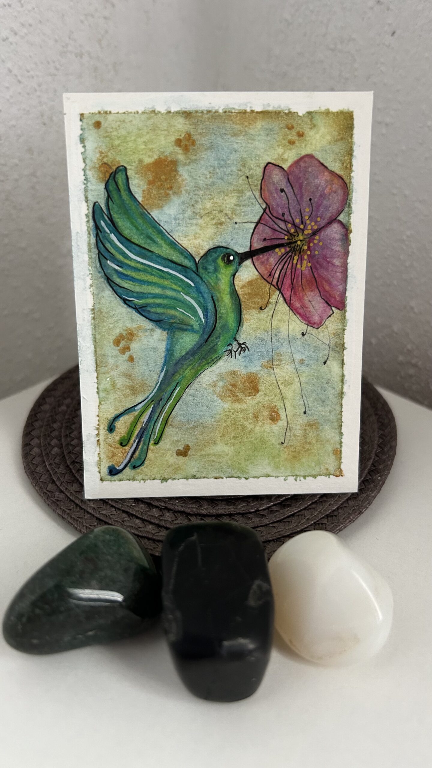 Original miniature painting “The Hummingbird Alchemist” by Nia Dannai, green hummingbird drinking nectar from hibiscus-like flower on metallic gold background, mixed media